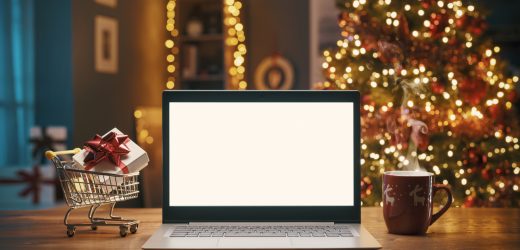 Christmas shopping online at home, laptop with blank screen and miniature shopping cart with a gift inside, holidays and sale concept