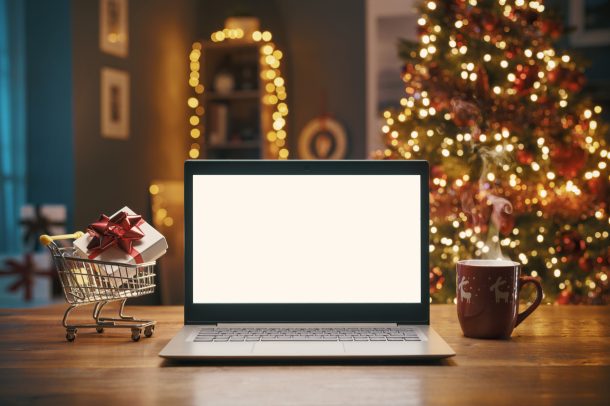 Christmas shopping online at home, laptop with blank screen and miniature shopping cart with a gift inside, holidays and sale concept